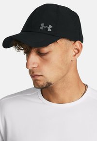 Schwarze Sportmütze aus leichtem Material, mit gebogenem Schirm, genähten Details und einem reflektierenden Logo auf der Vorderseite.