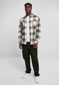 Rutede flannel skjorte i sort og hvid, knap- klassisk stil med brystlommer, båret over en hvid t-shirt og parret med sorte cargo bukser.