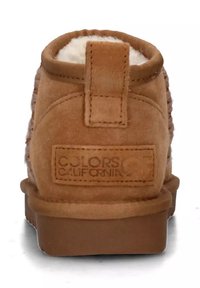 Stivaletto in suede marrone con una morbida foderatura in pelliccia bianca, suola piatta e un occhiello sul retro. Presenta un design testurizzato e un'etichetta con il logo.
