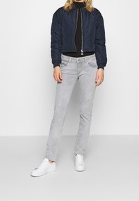 Granatowa pikowana kurtka bomberka, czarny top z wysokim kołnierzem, jasnoszare dżinsy z przetarciami oraz białe sneakersy.