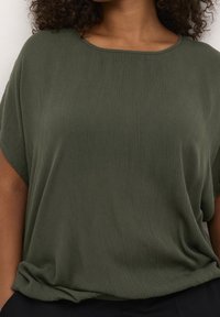 Olivengrøn kortærmet top med en afslappet pasform, der har en bred halsudskæring og en struktureret stof med subtile lodrette linjer.