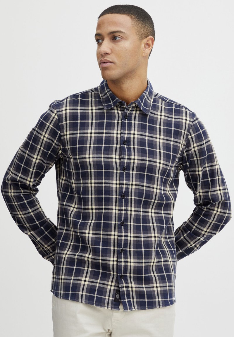 Cămașă cu mâneci lungi în carouri navy și crem, cu un guler clasic și o croială slim; prezintă nasturi în față și un tiv curbat.
