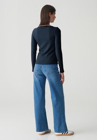 Schwarzes, geripptes Langarmoberteil kombiniert mit hoch taillierten blauen Jeans im weit geschnittenen Style und weißen Sneakers mit marineblauen Streifen.