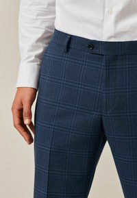Navy plaid trousers with blue and gray lines, featuring a button closure and a textured fabric, designed for a fitted look.