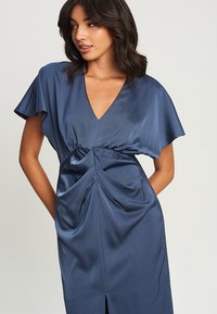 Marineblaues Satin-Kleid mit V-Ausschnitt, kurzen, schwingenden Ärmeln und geraffter Taille. Verfügt über einen Schlitz vorne und eine glatte, fließende Textur.