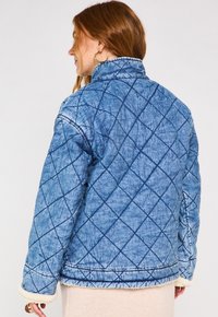 Giacca in denim trapuntato di colore azzurro chiaro con motivo a diamante. Presenta un colletto alto e una fodera in shearling ai polsini e all'orlo. Tessuto testurizzato.