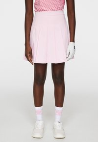 Rosa plisserad golfkjol med hög midja, kombinerad med vita sportskor och rosa-accenterade strumpor. Materialet verkar glatt och lätt.