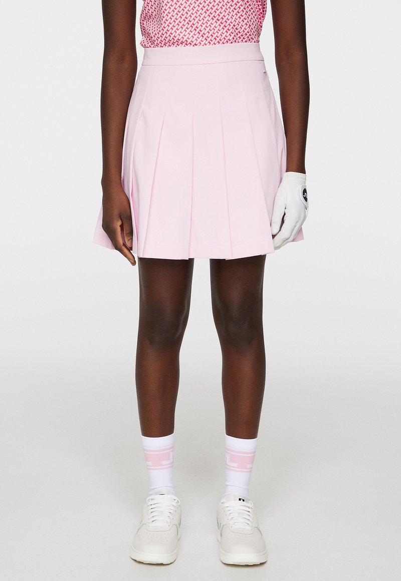 Rosa plisserad golfkjol med hög midja, kombinerad med vita sportskor och rosa-accenterade strumpor. Materialet verkar glatt och lätt.