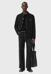 Czarna kurtka z kieszenią z przodu, w połączeniu z ciemnymi dżinsami i teksturowaną czarną torbą. Model nosi czarne buty z białymi akcentami.