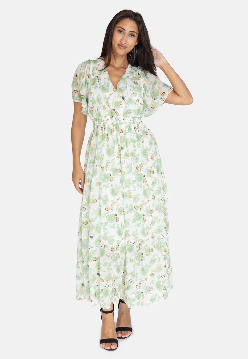 Robe maxi en tissu vert clair, ornée de motifs floraux, dotée d'un décolleté en V, de manches courtes et d'une taille élastique. Portée avec des sandales à talons noires.