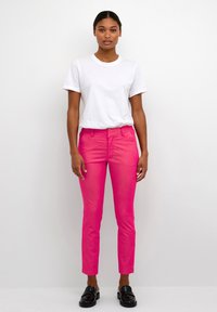 Pantaloni aderenti rosa con tasche anteriori, design a gamba dritta, abbinati a una t-shirt bianca a manica corta. Scarpe nere completano l'outfit.