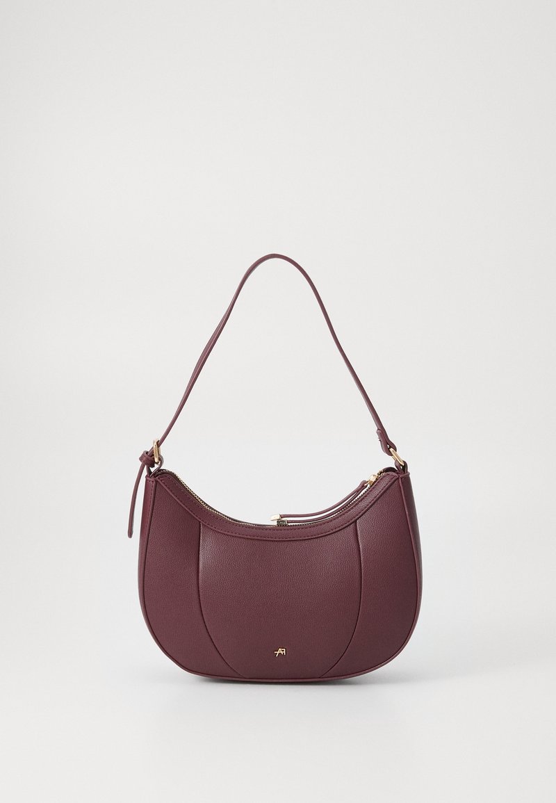Sac à épaule en cuir violet foncé avec fermeture éclair dorée et petit logo doré sur le devant, façonné avec des coutures courbes et une seule bandoulière.