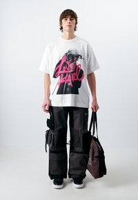 Witte oversized t-shirt met een grafische print in roze en zwart. Zwarte cargobroek met meerdere zakken. Zwarte sneakers en een zwarte tas.