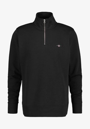 Sudadera negra con cremallera y cuello alto, hecha de una tela suave. Presenta puños y dobladillo acanalados, con un pequeño logo en el lado izquierdo del pecho.