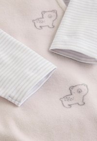 Harmaan karhun graafikilla varustettu vaaleanpunainen fleecekangas, sekä raidalliset valkoiset ja beige pitkät hihat, joissa on käänteet.