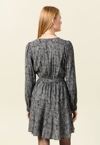 Schwarzes Blumen Kleid mit langen Ärmeln, tailliertem Bund und plissiertem Rock. Hat ein Rosenmuster und einen lockeren Schnitt. Rückansicht gezeigt.