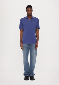 Purple polo shirt with a collared neckline, paired with light blue straight-leg jeans. Simple design, crafted from textured fabric. Black shoes.