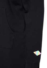 Sweat-shirt noir en tissu texturé avec une poche à l'avant. Présente un logo irisé en forme de diamant sur la manche.