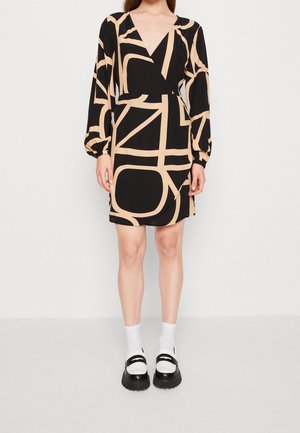 Schwarzes Kleid mit großen beigen abstrakten Linien, tiefem V-Ausschnitt, langen Puffärmeln und taillierter Passform. Getragen mit weißen Socken und schwarzen Schuhen.