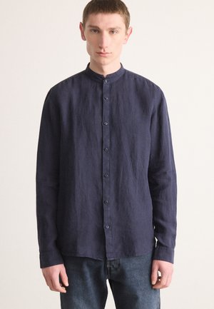 Navy blue long-sleeve shirt with a mandarin collar, textured linen fabric, and button-down front; paired with denim jeans.