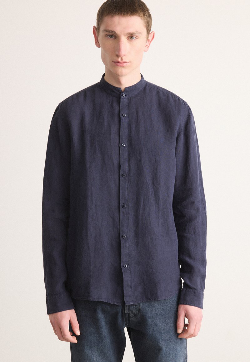 Marineblå langermet skjorte med mandarin krage, teksturert linestoff og knappestolpe; kombinert med denimjeans.