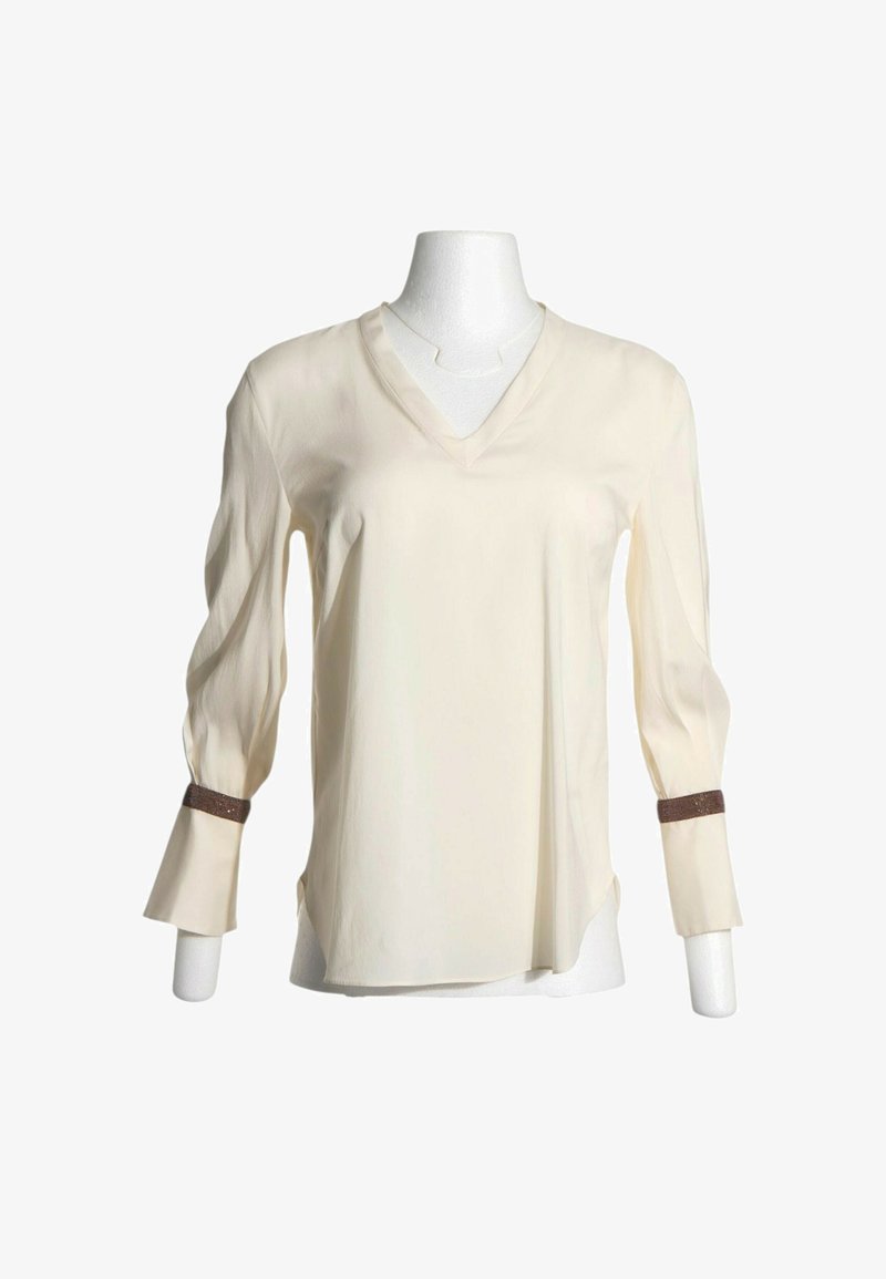 Blouse crème à manches longues avec encolure en V et bandes décoratives marron au-dessus des poignets, présentée sur un buste de mannequin blanc.