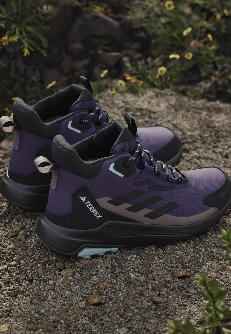 Zapatos de senderismo morados con suela de goma negra, parte superior texturizada y acentos blancos. Cuentan con cordones resistentes y pestañas en el talón.