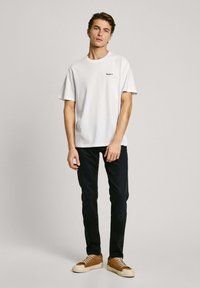 Vit bomull t-shirt med kort ärm, med en liten blå logotyp. Kombinerad med mörka jeans och ljusbruna sneakers med vita sulor.