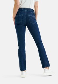 Jeans in denim blu scuro con gamba dritta, vita alta e due tasche posteriori. Abbinati a sneaker bianche su uno sfondo neutro.
