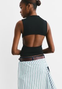 Schwarzes ärmelloses Top mit offenem Rückendesign, kombiniert mit einem gestreiften Wickelrock in Weiß und Grün. Glatte Textur und figurbetonte Silhouette.