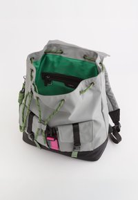 Mochila gris con interior verde, base negra y herrajes negros. Presenta un cierre de cordón, correas ajustables y bolsillos exteriores.