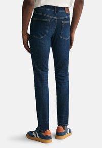 Jeans in denim blu scuro con una vestibilità slim, dotati di due tasche posteriori, cuciture a contrasto e una patch in pelle marrone sulla vita.