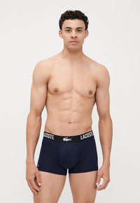 Sötétkék boxeralsó fekete gumírozott derékkal, amelyen a Lacoste logó látható. Az anyag lágy és sima tapintású.