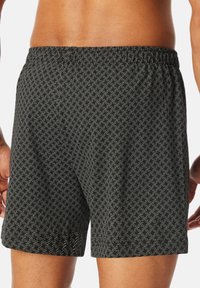 Svarta badbyxor med ett geometriskt vitt mönster, elastisk midja och normal passform. Materialet verkar lätt och har en mjuk textur.