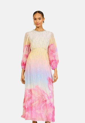 Vrouw draagt een lange pastel ombre jurk met roze bloemmotieven, pofmouwen en zilveren pailletten details, staand tegen een witte achtergrond.