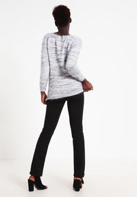 Grå fluffig tröja med lös passform och långa ärmar, i kombination med svarta tajta jeans och öppna klackskor. Tröjan har ett strukturerat mönster.