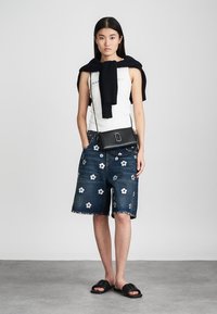 Shorts di jeans con ricami floreali, abbinati a un top bianco e una borsa a tracolla nera. Maglione lavorato a maglia appoggiato sulle spalle.