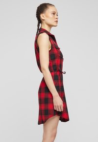 Abito a scacchi rosso e nero con design senza maniche, vita regolabile con cordoncino e orlo che scende ai lati.