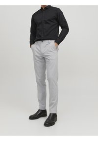 Camicia nera con bottoni abbinata a pantaloni grigi chiari su misura e stivaletti neri alla caviglia; design elegante con tessuto texture e tasche.