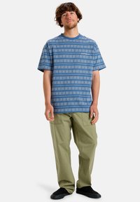 Short-sleeve blue patterned shirt with a subtle design, paired with loose olive green trousers and black footwear.