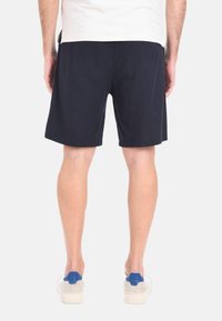 Shorts blu navy realizzati in tessuto leggero, con taglio dritto e tasche laterali. Indossati con scarpe da ginnastica chiare con accenti blu.