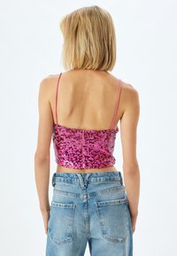 Pink sequined crop top med tynde stropper, der har et tætsiddende design. Kombineret med lys blå højtaljede jeans, der viser et afslappet look.