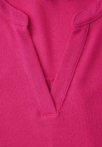 Primo piano di un tessuto rosa lavorato a maglia con un collo a V profondo che mostra motivi a maglia strutturati e bordi piegati.