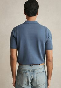 Cămașă polo cu mânecă scurtă și guler, dintr-un material bleu fin. Are manșete ribbed și accente texturate verticale pe umeri. Poartă cu blugi deschiși la culoare.
