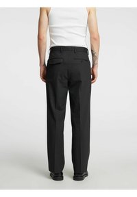 Sorte skreddersydde bukser med rette ben, med to baklommer og beltehemper, kombinert med en tettsittende hvit tanktop.