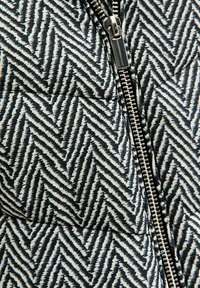 Czarna i biała kurtka puchowa w wzór zygzakowy z metalowym zamkiem błyskawicznym z przodu i wyściełaną teksturą dla zapewnienia izolacji.