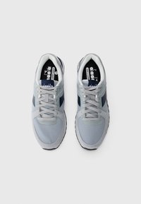 Light grey sports shoes with navy accents, mesh upper, and round laces. Features padded collar and textured rubber sole for traction.