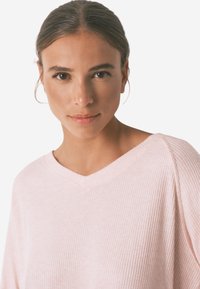 Lichtroze geribde trui met een V-hals en lange mouwen, voorzien van een zachte textuur en een ontspannen pasvorm. Ideaal voor laagjes of casual draag.