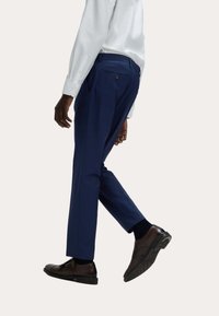 Granatowe spodnie z gładkiego materiału, z tylną kieszenią i szlufkami na pasek, w połączeniu z ciemnobrązowymi eleganckimi butami.