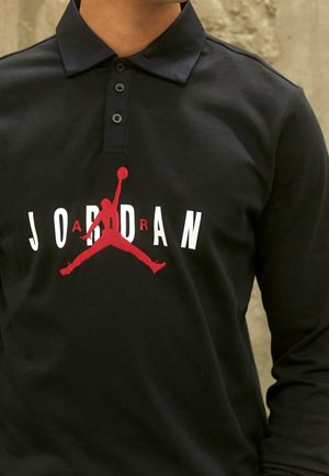 Schwarzes Langarm-Poloshirt mit rotem Jumpman-Logo und weißem sowie rotem "JORDAN"-Schriftzug auf der Brust, getragen von einer Person.